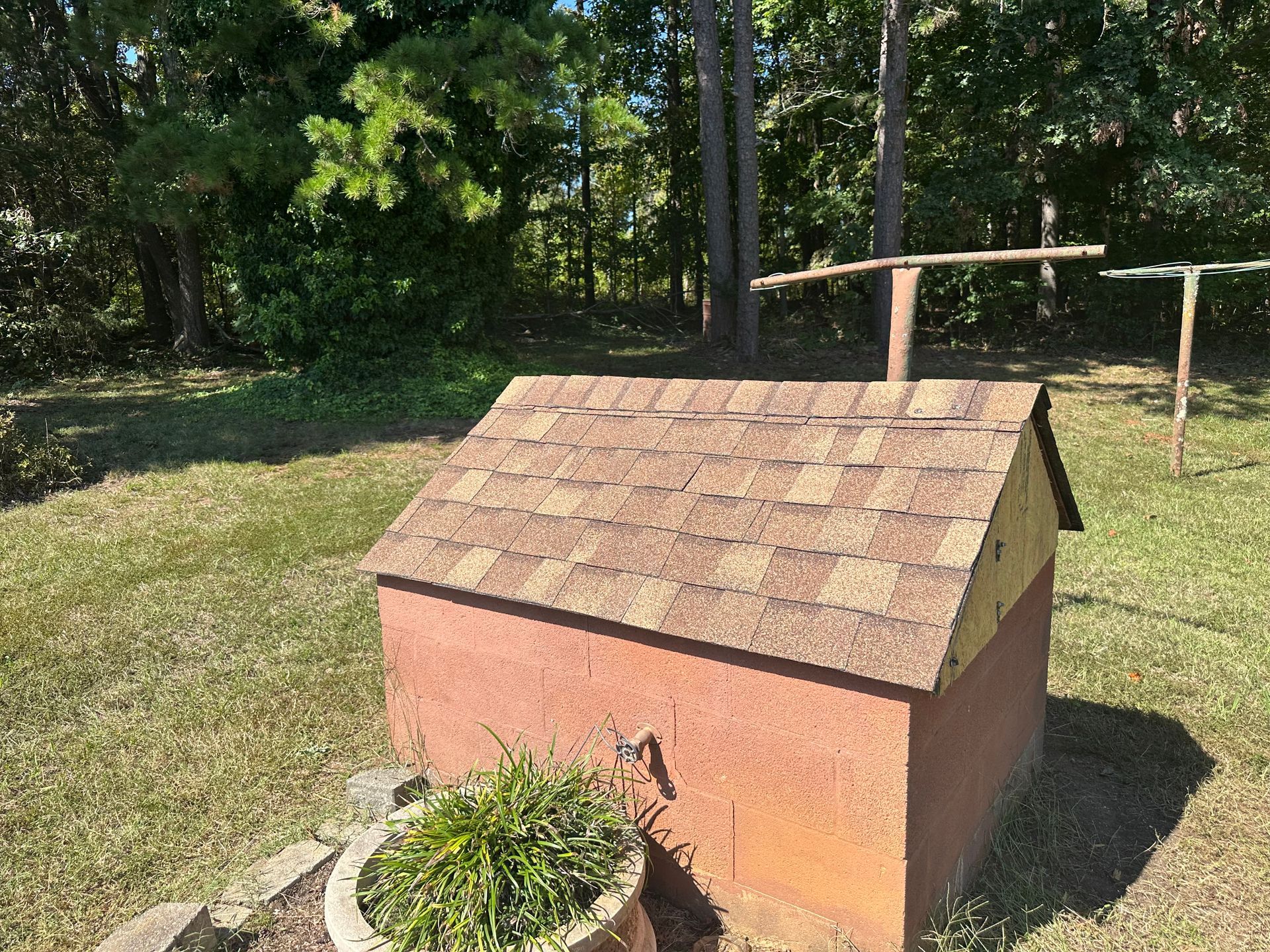 A small brick building with a roof is sitting in the middle of a grassy field.
