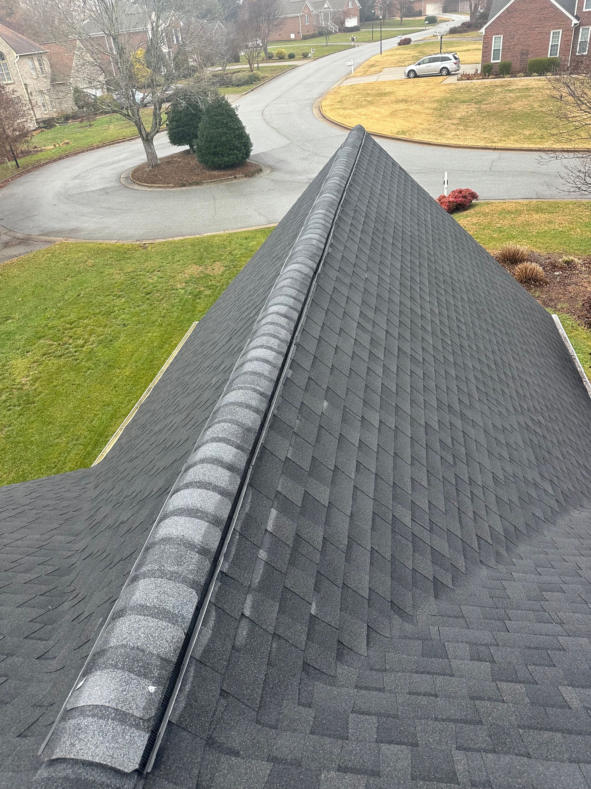 An aerial view of a roof in a residential area with a driveway in the background.