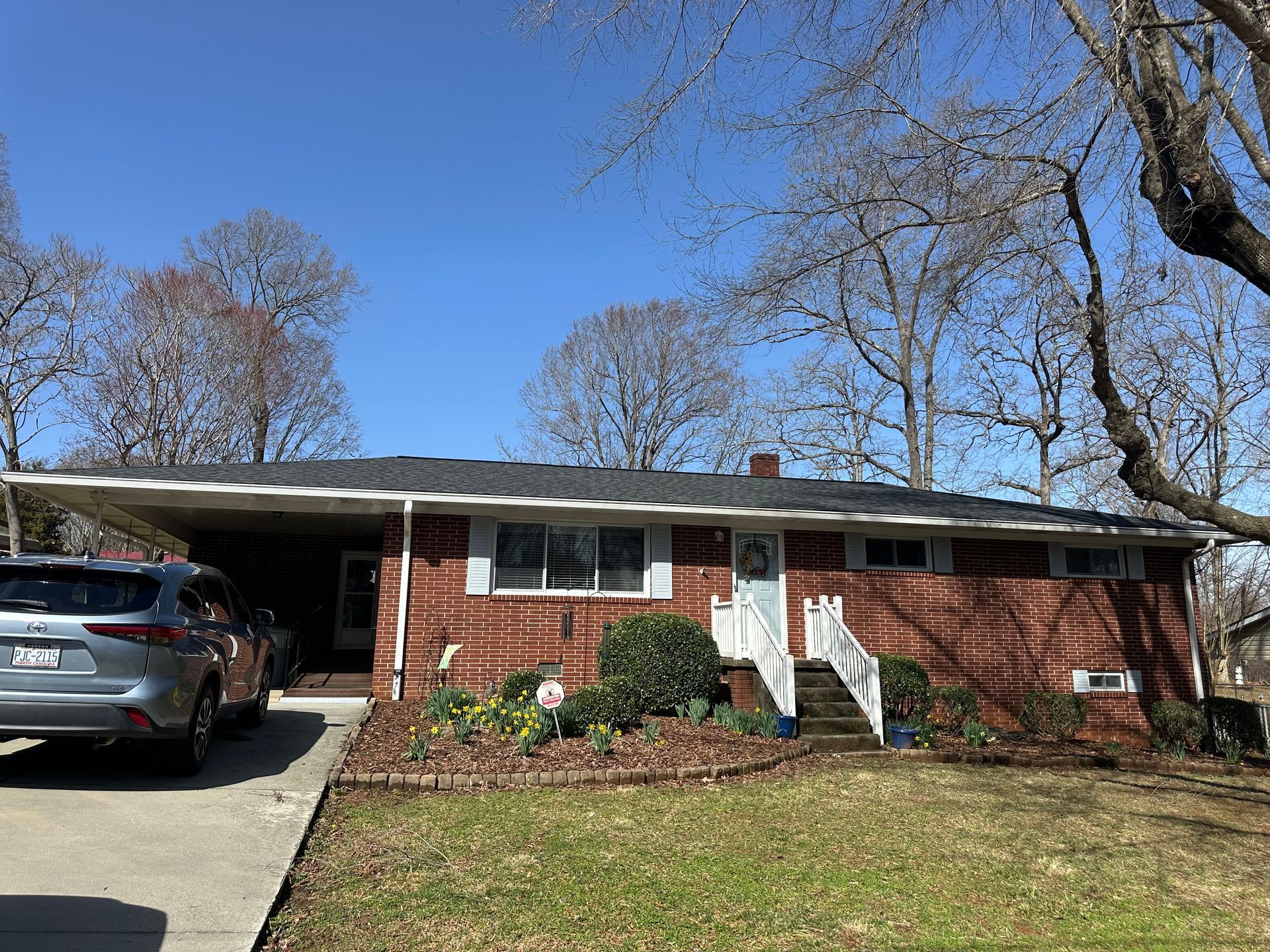 A car is parked in front of a brick house.
