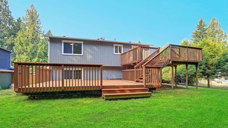 Wooden deck attached to a gray house with stairs and railings in a grassy backyard