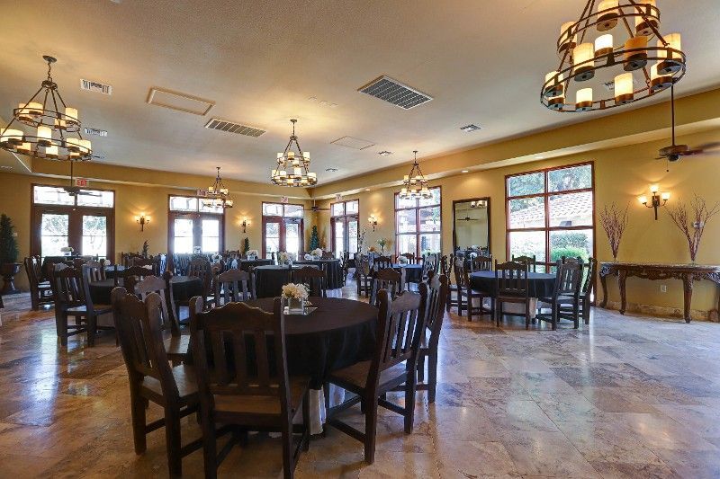 Dining room with round tables, brown chairs, chandeliers, and arched windows.
