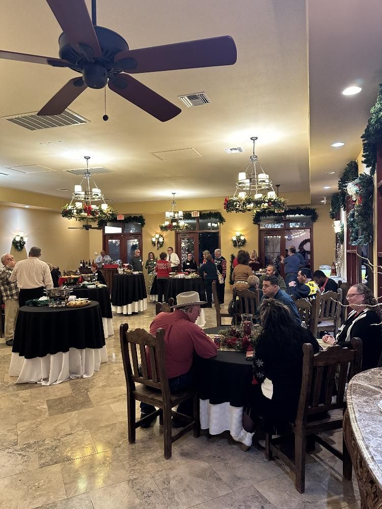 People at a holiday party in a warmly lit room with tables, festive decorations, and a ceiling fan.