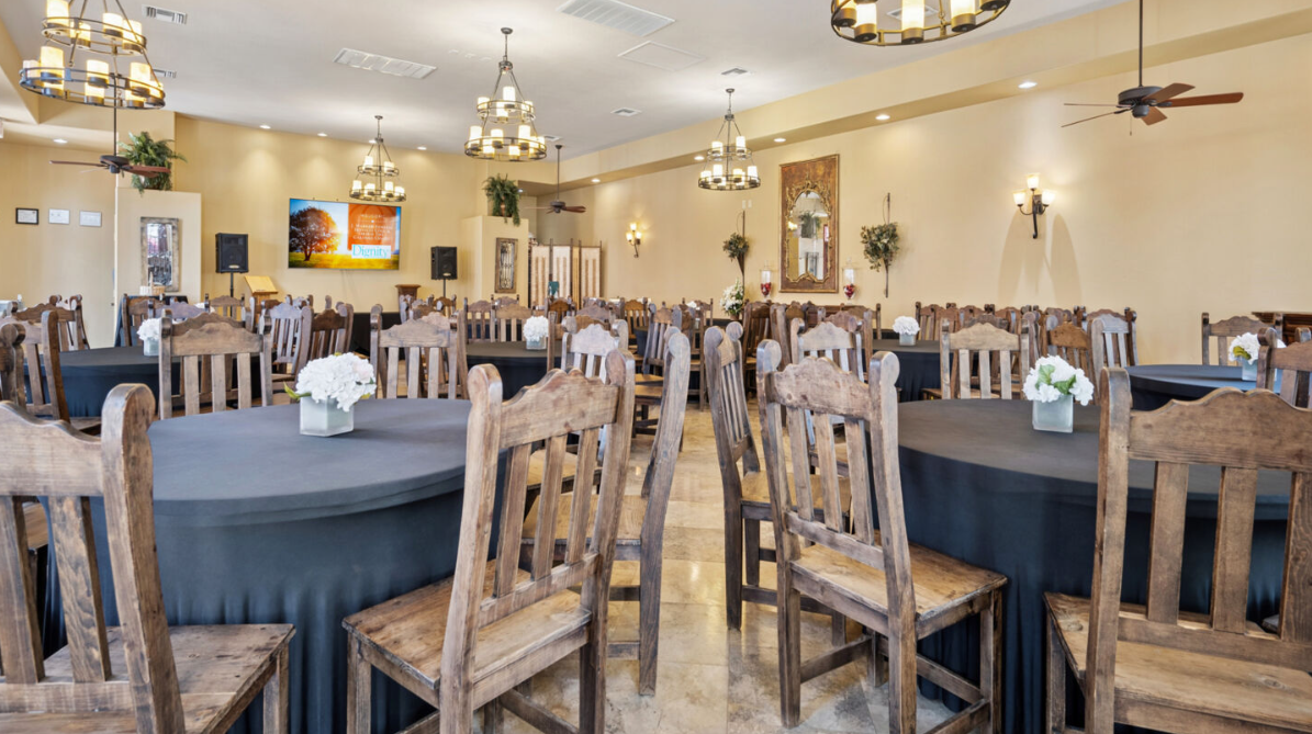 Dining room with round tables, black tablecloths, rustic wooden chairs, and chandeliers.