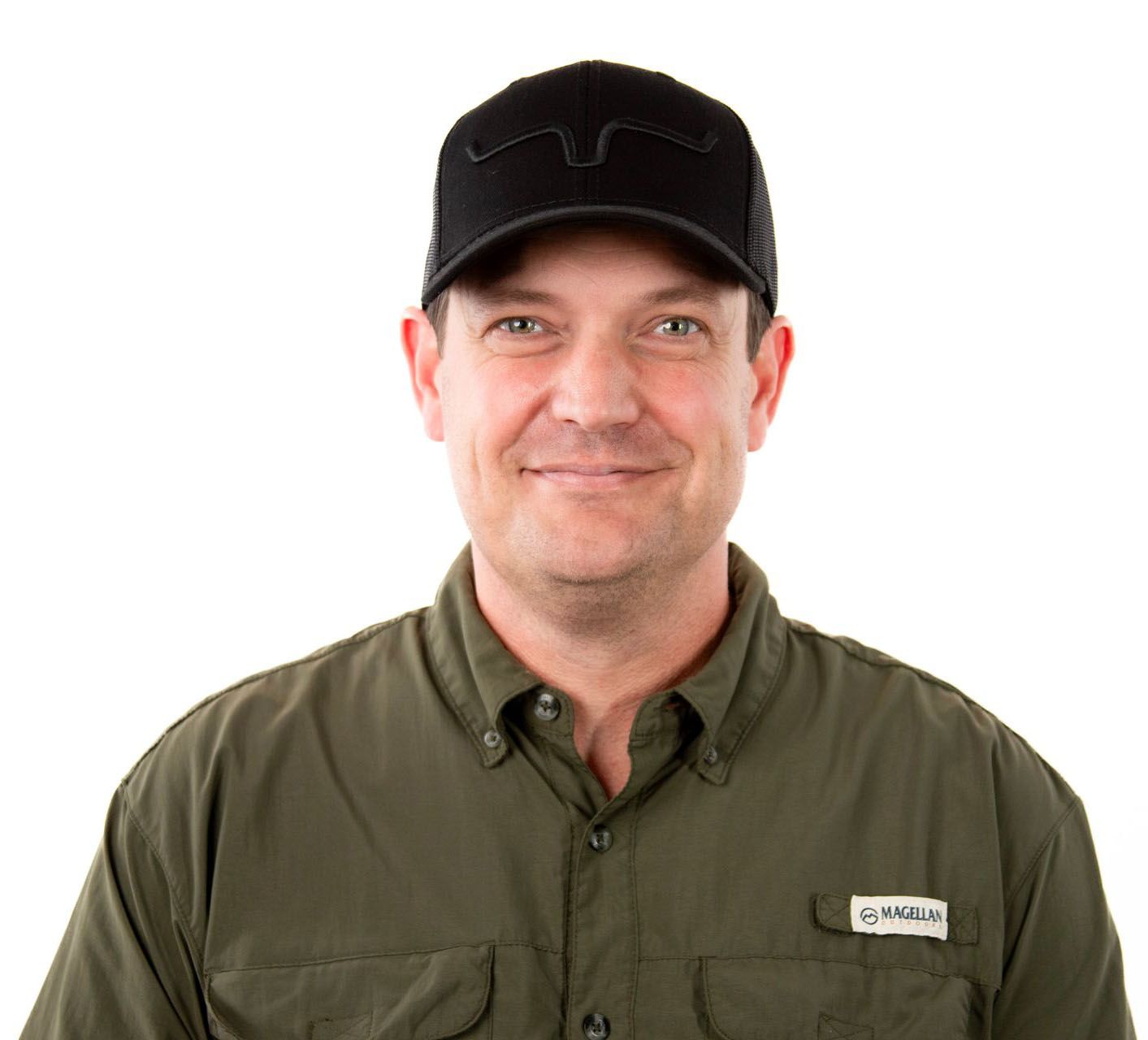 A man wearing a green shirt and a black hat is smiling