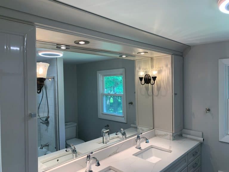 Bathroom vanity with large mirror, white countertop, sconces, and a window with daylight outside