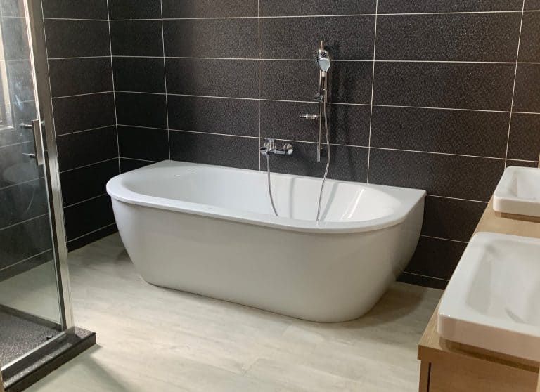 Modern bathroom with a freestanding white tub, dark tile walls, and a glass shower enclosure