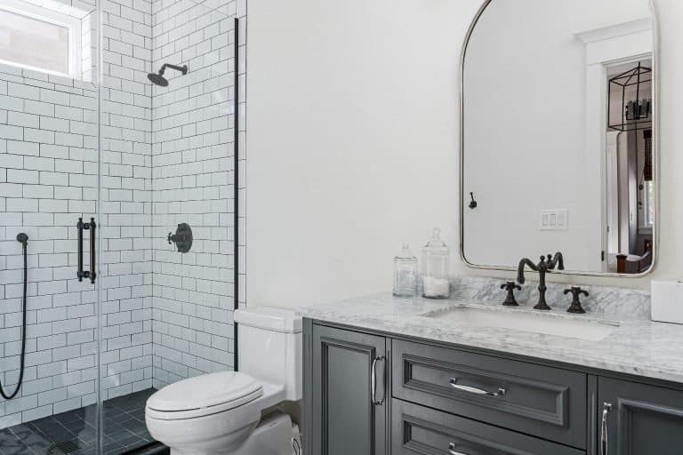 Modern bathroom with white subway tile, walk-in shower, toilet, and gray vanity with arched mirror