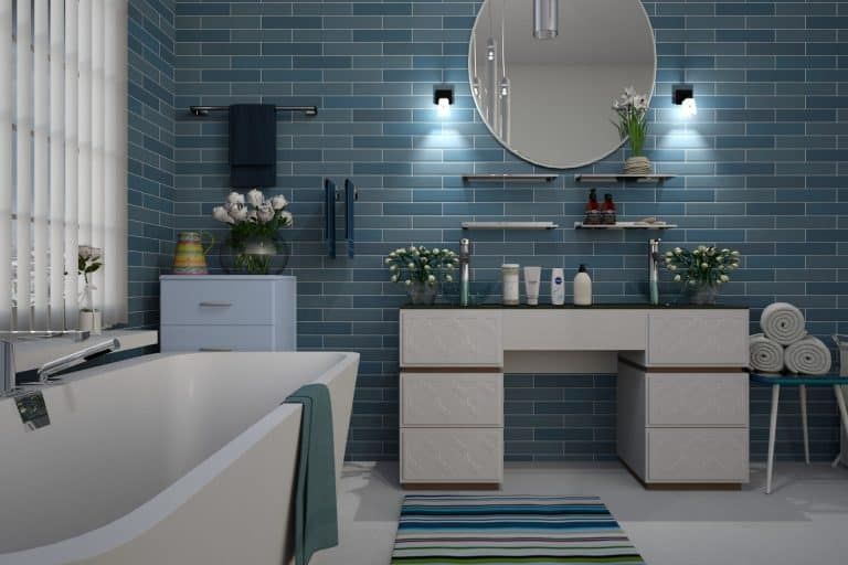 Modern blue bathroom with freestanding tub, vanity, round mirror, and striped rug