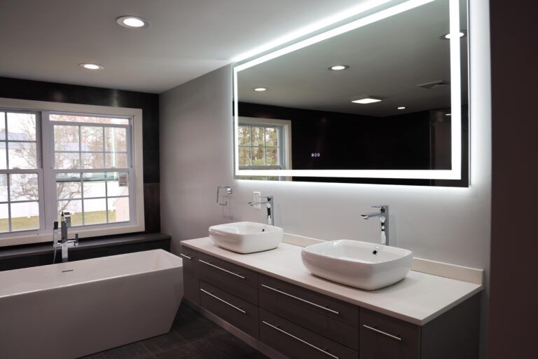 Modern bathroom with a tub, double sinks, and a large backlit mirror