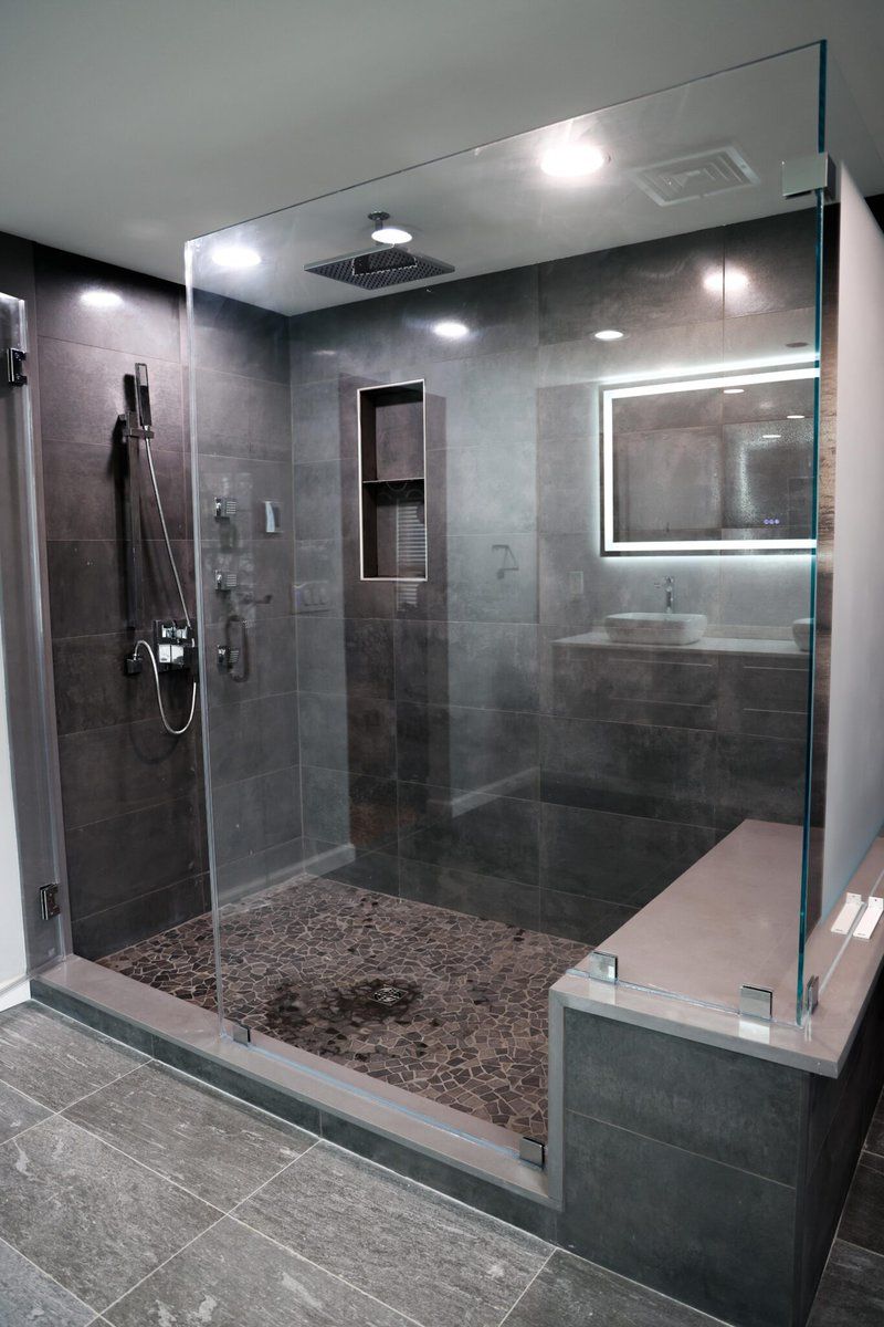 Modern glass shower enclosure with gray tile walls, pebble floor, and built-in bench in a bathroom