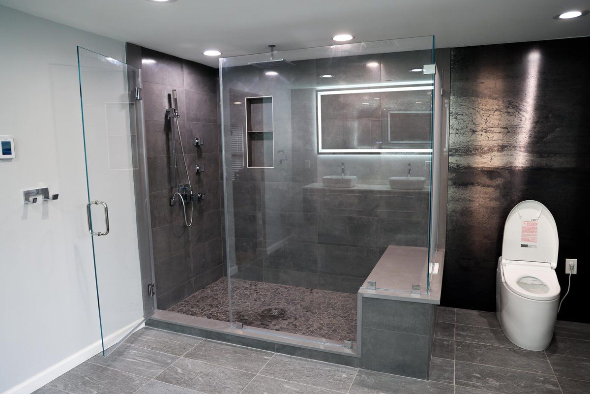 Modern bathroom with glass shower enclosure, dark tile walls, and a toilet.