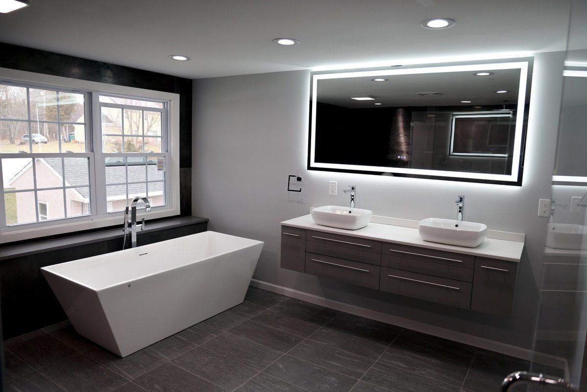 Modern gray bathroom with freestanding tub, double vanity, large mirror, and window.