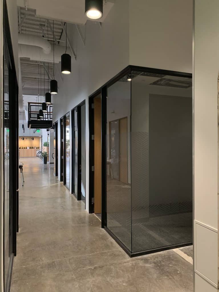 Empty modern office hallway with glass-walled rooms and black pendant lights