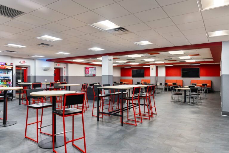 Modern cafeteria with red tables and stools under bright fluorescent lights