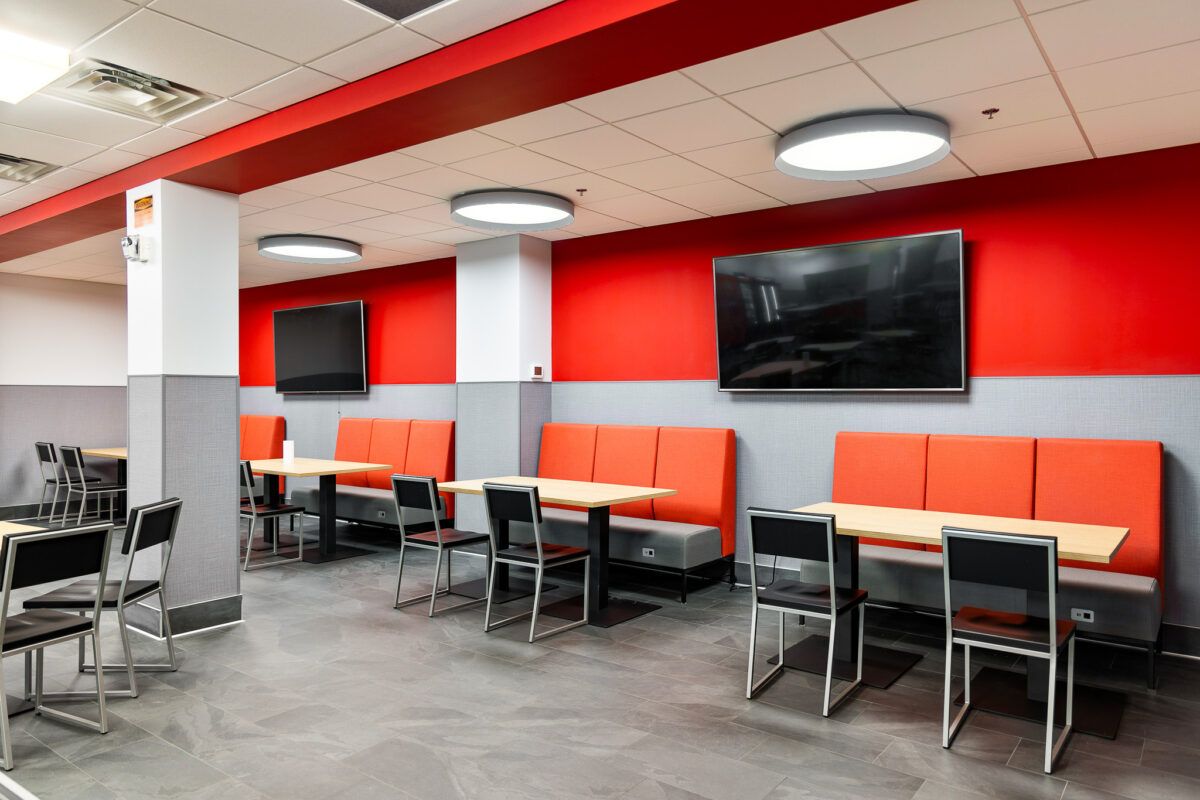 Empty fast-food dining area with orange booths, black tables, wall TVs, and red-and-white decor