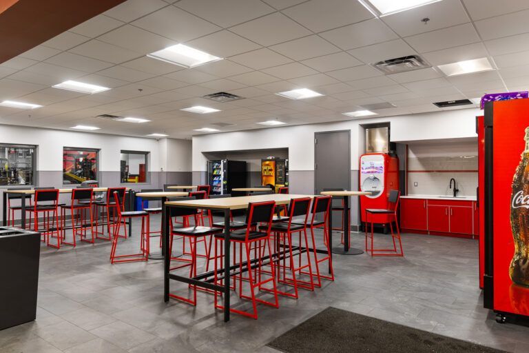 Empty fast-food dining area with red tables, stools, and bright overhead lights