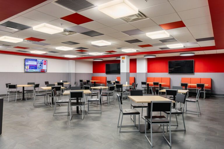Empty modern classroom with tables and chairs, red-and-gray walls, and a wall-mounted TV