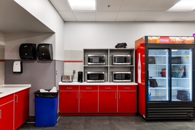 Red break room with coffee station, microwave ovens, and glass-door refrigerator with beverages.