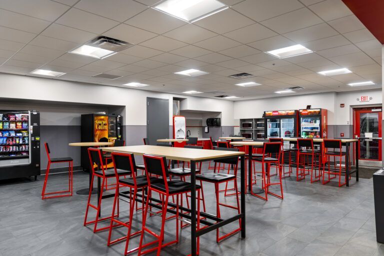Empty modern cafeteria with red stools, high tables, and vending machines under bright ceiling lights