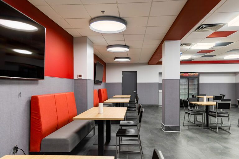 Modern restaurant seating area with red booths, gray tables, and pendant lights