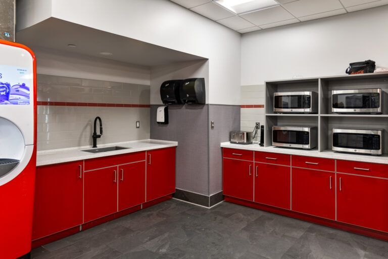 Modern break room with red cabinets, sink, and stainless steel microwave ovens