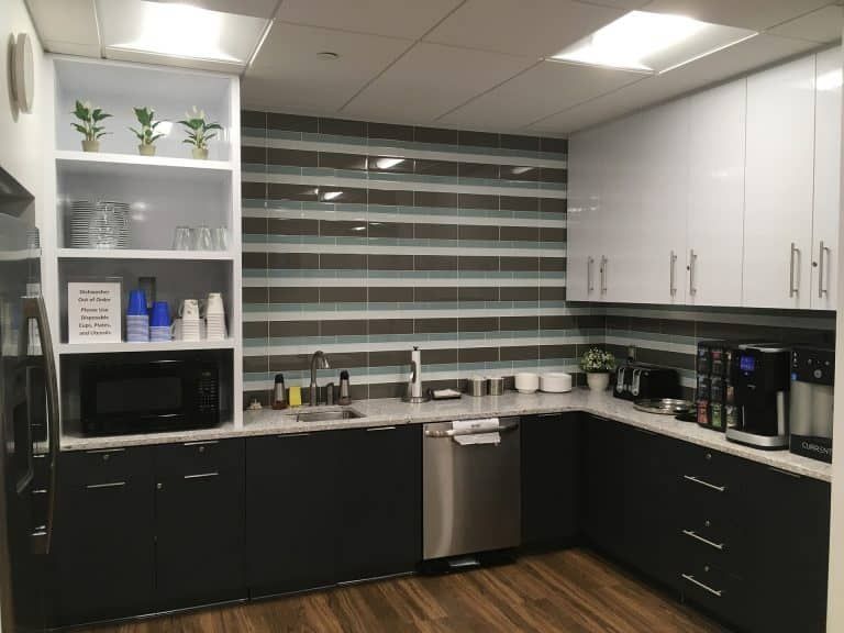 Modern office kitchenette with black lower cabinets, white upper cabinets, sink, microwave, and coffee maker