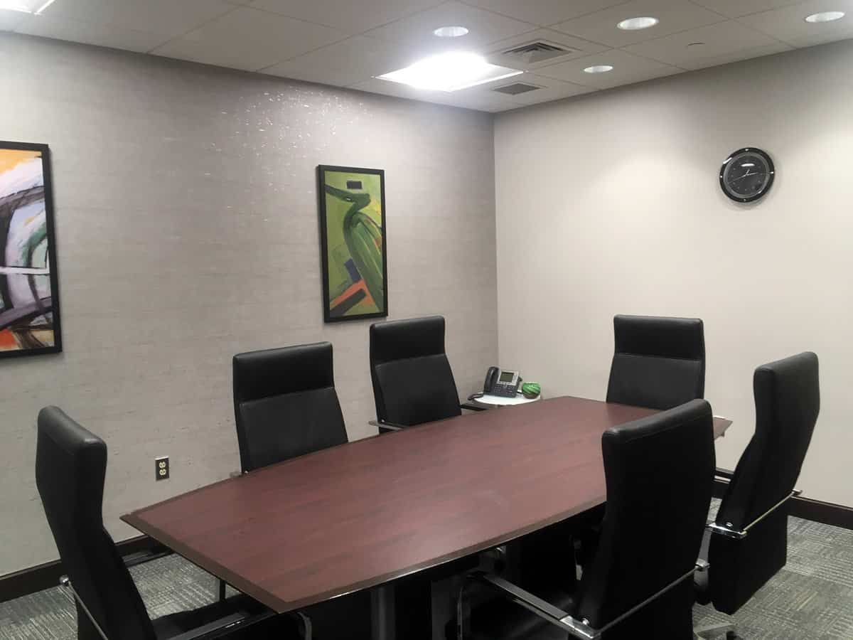 Conference room with a long wooden table, black chairs, framed wall art, and a wall clock.
