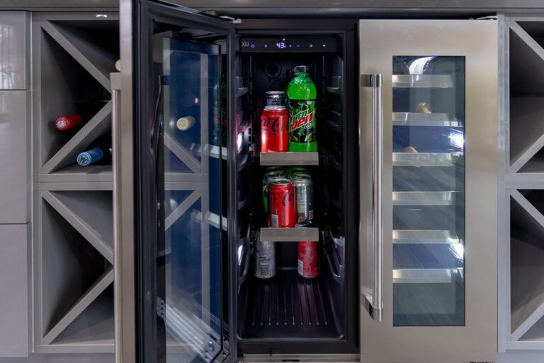 Built-in wine cooler with glass door, holding bottles and cans on metal shelves.