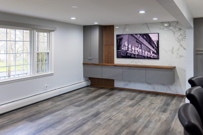Empty modern room with gray wood floor, large window, wall-mounted TV, and built-in shelves