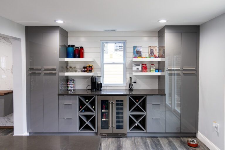 Modern gray kitchen with open shelving, stainless sink, wine storage, and a central window.