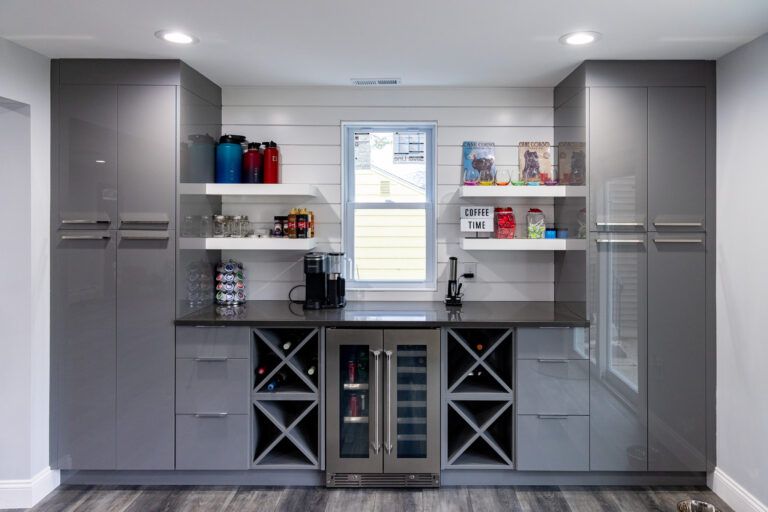Modern gray home bar with built-in shelves, cabinets, wine rack, and small sink.