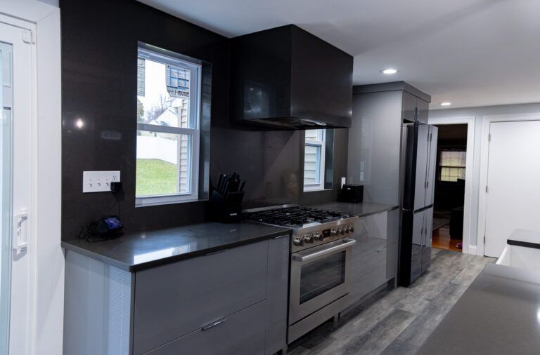 Modern kitchen with dark cabinets, stainless stove, gray counters, and a hallway beyond