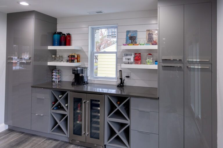Modern gray wet bar with cabinets, wine fridge, shelves, and a window above the sink