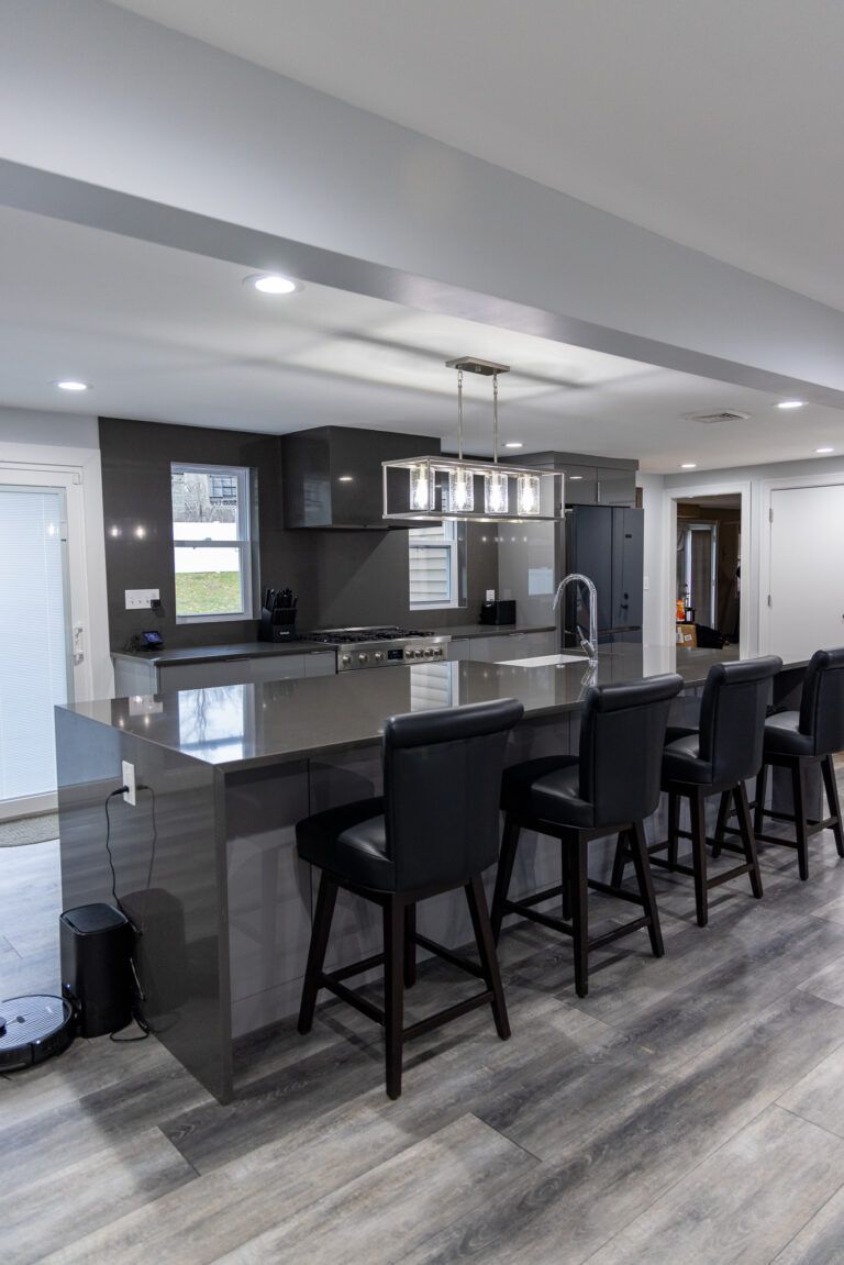 Modern kitchen with gray island, black barstools, pendant lights, and stainless steel appliances