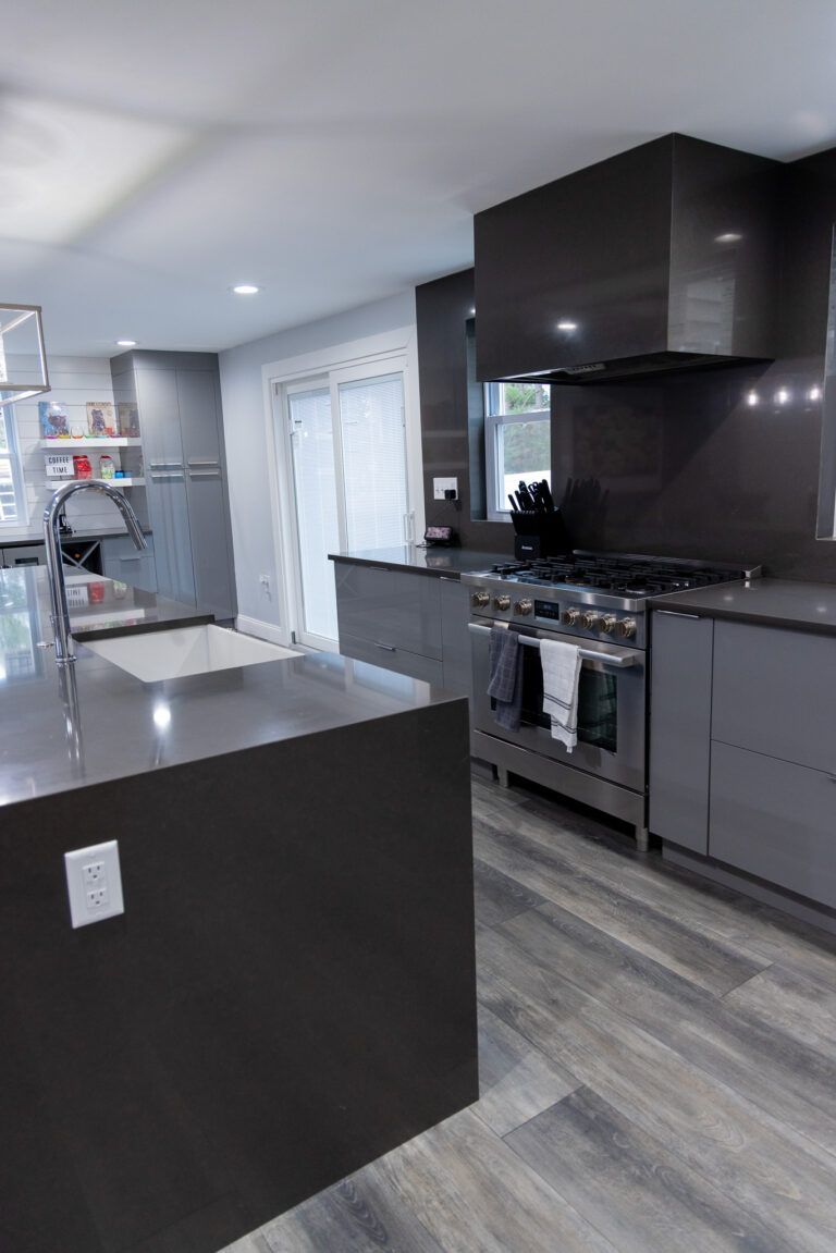 Modern kitchen with dark gray cabinets, stainless stove, and light wood flooring
