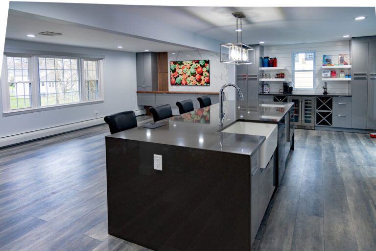 Modern kitchen with large island, bar stools, stainless appliances, and gray wood flooring