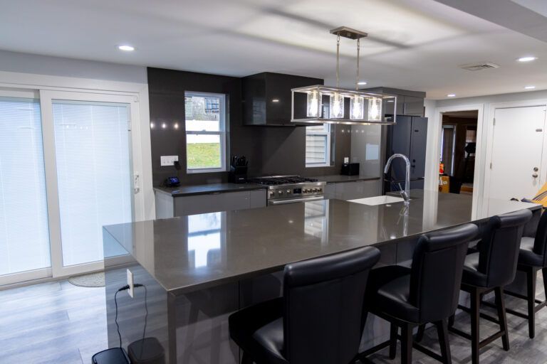 Modern kitchen with a large island, dark stools, and stainless steel pendant lights