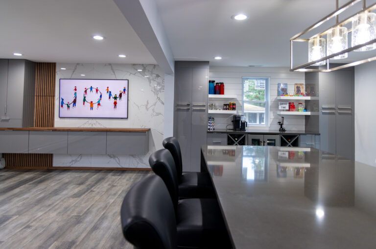 Modern kitchen with a glossy island, black bar stools, and a wall-mounted TV in an open living area