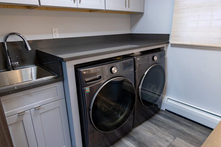 Laundry nook with black front-loading washer and dryer under a dark countertop beside a sink