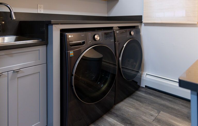 Black washer and dryer in a small laundry nook with gray cabinets and wood flooring