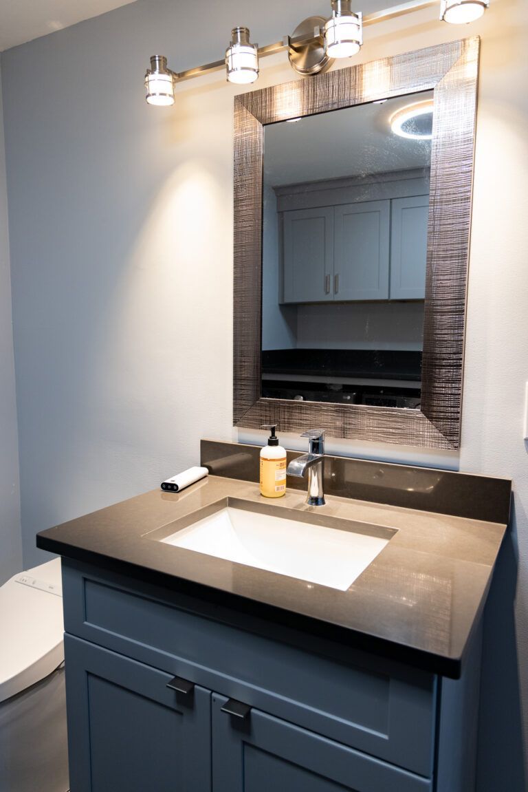 Bathroom vanity with dark countertop, white sink, lit mirror, and wall-mounted light fixtures