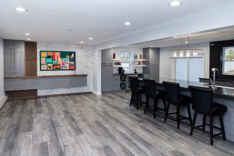 Modern open-plan room with gray flooring, bar seating, kitchen area, and colorful wall art.