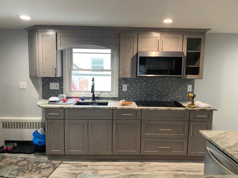 Modern kitchen with gray cabinets, window over sink, black backsplash, and microwave above the counter