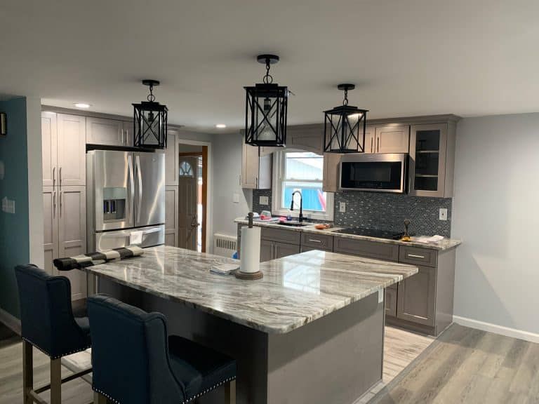 Modern kitchen with gray island, bar stools, pendant lights, and stainless steel appliances