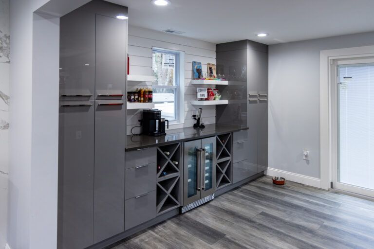 Modern home bar area with gray cabinets, wine rack, shelves, and wood-look flooring