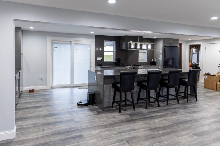 Modern open-concept kitchen with gray floors, dark cabinets, island, and barstools