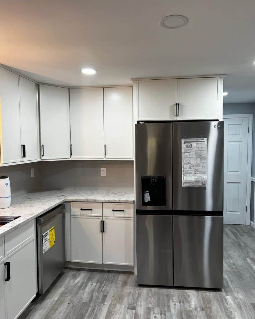 Modern kitchen with white cabinets, stainless steel refrigerator, and gray flooring