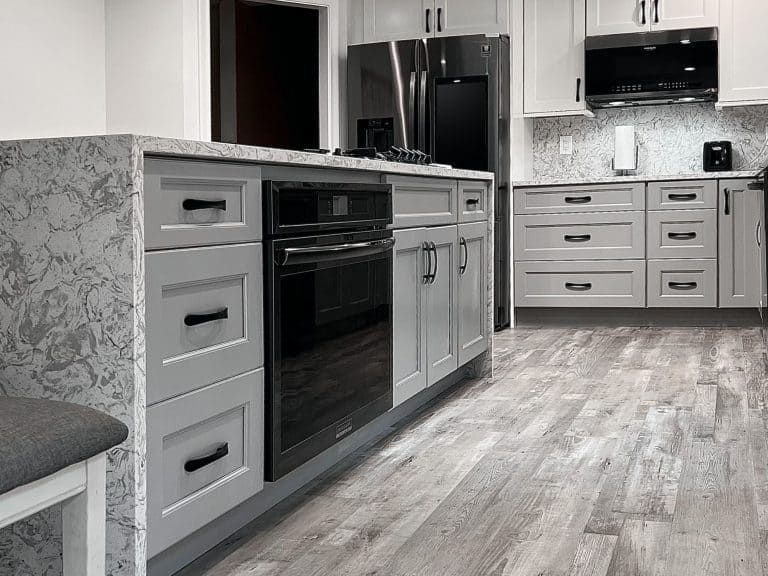Modern gray kitchen with island, stainless steel appliances, and light wood flooring