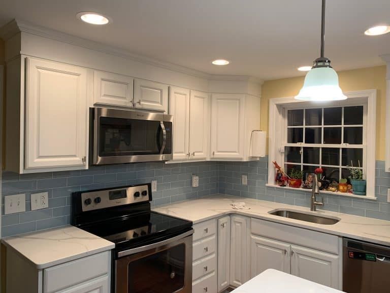 Modern kitchen with white cabinets, black stove and microwave, blue tile backsplash, and window over the sink.