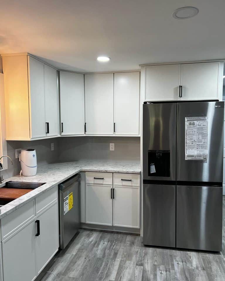 Modern kitchen with white cabinets, gray countertops, stainless steel fridge, and gray wood-look flooring.